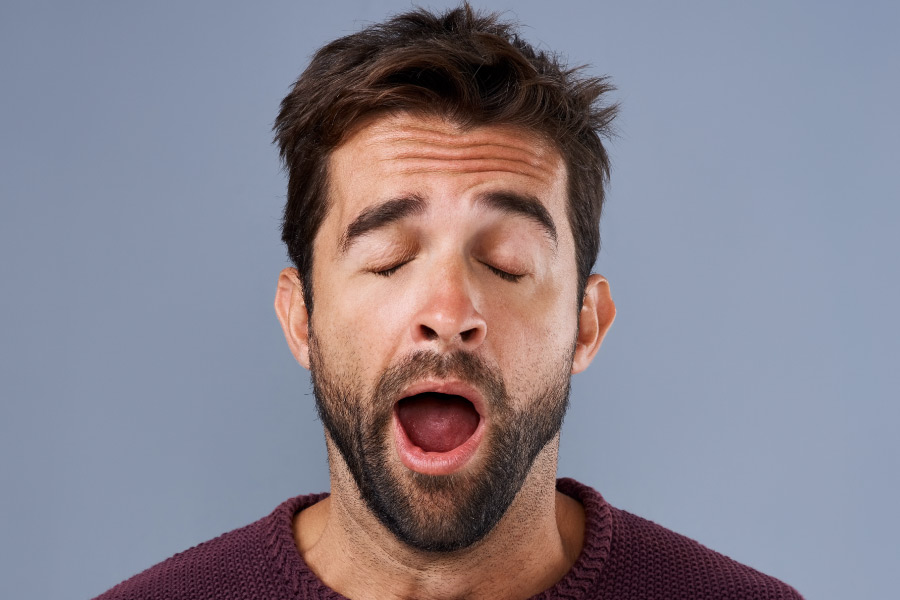 Brunette man with sleep apnea yawns because of daytime sleepiness and fatigue from poor quality sleep in Summerville