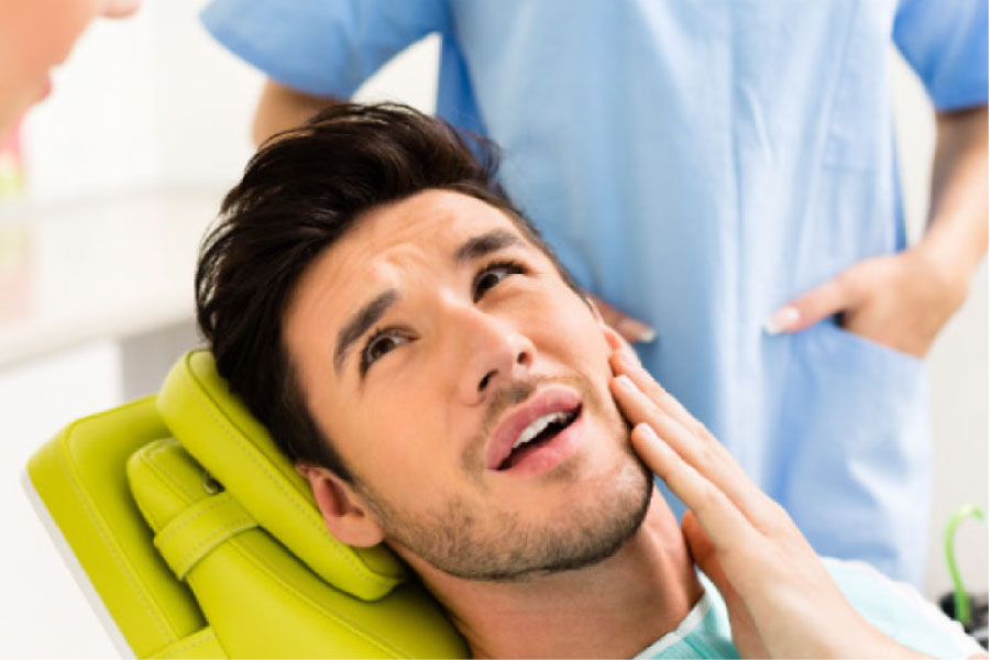 man in the dentist chair holds his jaw before a tooth extraction